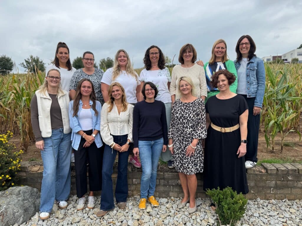 Gruppenfoto des Lehrerkollegiums der Grundschule Dormitz-Hetzles-Kleinsendelbach im Schuljahr 2026/2027, zwei Reihen vor einem Maisfeld